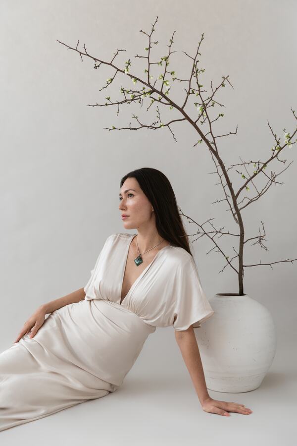 A patient seated in a cream silk dress beside a flowering branch